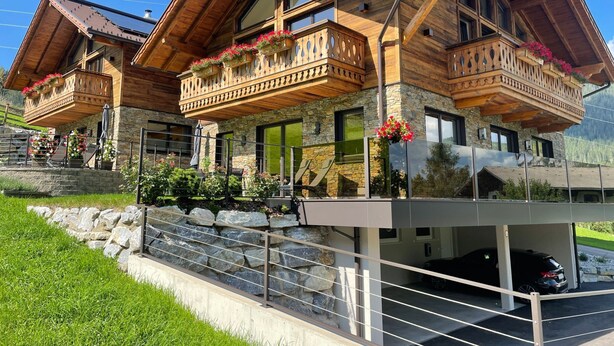 Eine Chalet mit Holzbalkonen, Steinmauern und einer Autoeinfahrt.