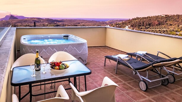 Un balcón con bañera de hidromasaje, una mesa con copas de vino y fruta, y sillones de descanso.