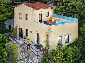 Ein zweistöckiges Gebäude mit Pool auf dem Dach, Steinstufen zum Eingang und Außenbereich mit Sitzgelegenheiten.