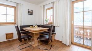 Un comedor con una mesa de madera y sillas negras, una ventana con cortinas y vistas a un paisaje nevado.