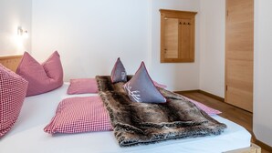 Un dormitorio con una cama cubierta por una manta a cuadros y almohadas, un armario de madera y una lámpara fijada a la pared.