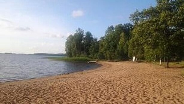Une plage de sable fin, avec une étendue d’eau calme, des arbres et un petit bateau.