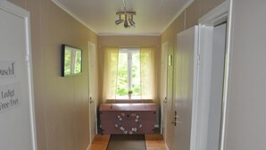 Un couloir doté d’un plancher en bois, d’un banc orné de motifs floraux, d’une fenêtre avec des rideaux et d’un ventilateur de plafond.