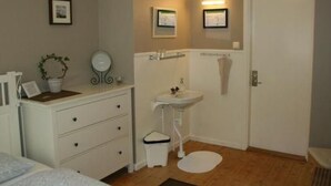 Une chambre à coucher avec un lit, une commode, un miroir, une petite plante et une porte blanche.