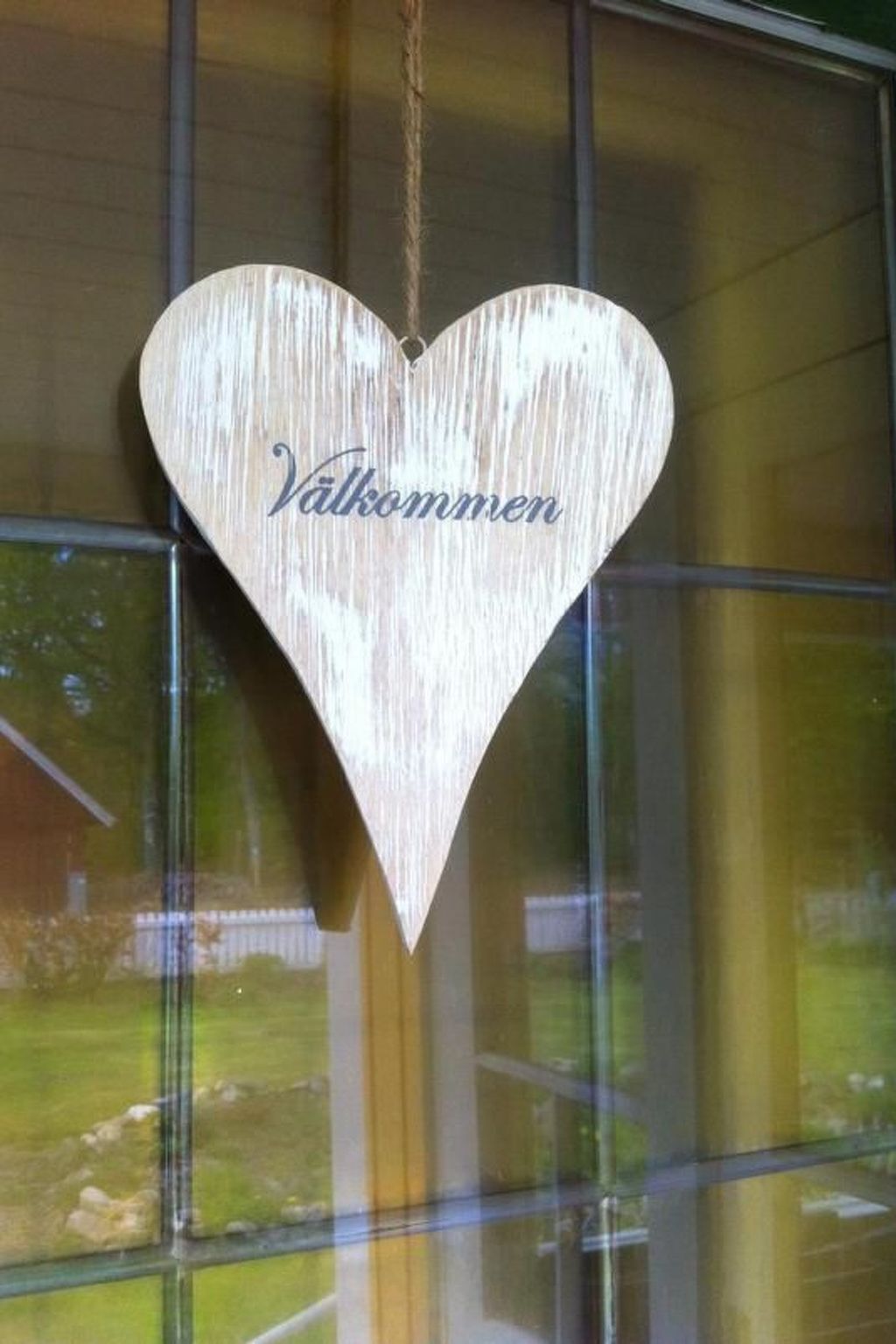 En hjärtformad trädekoration med ordet ”Välkommen” hängande i ett fönster.