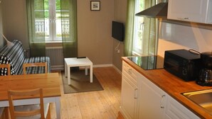 Une cuisine compacte avec un plan de travail en bois, un four à micro-ondes et une machine à café. On y trouve une petite table et une chaise dans l’espace repas, ainsi qu’un radiateur placé sous une fenêtre.