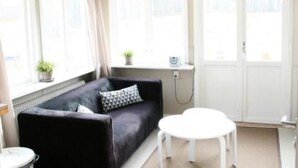 Une pièce avec un canapé noir, une petite table blanche et une fenêtre avec des rideaux.