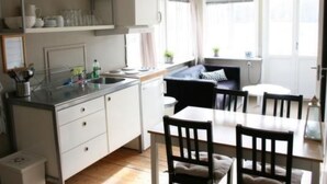 Une cuisine de taille réduite, avec des meubles blancs, un plan de travail et un coin repas comprenant une table et des chaises.