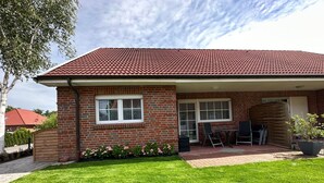 A single-story house with a red-tiled roof, brick exterior, and a covered patio area with outdoor furniture. - Gemütliches Ferienhaus mit Garten und Terrasse by Interhome (Norden)