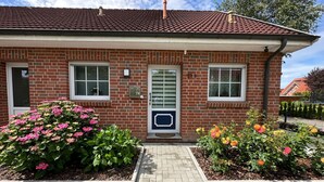 A two-story brick building with a red-tiled roof, a front door, two windows, and a small porch area with potted plants. - Gemütliches Ferienhaus mit Garten und Terrasse by Interhome (Norden)