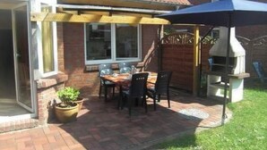 Eine Terrasse mit Tisch und Stühlen, ein Grill und ein überdachter Bereich mit einem blauen Sonnenschirm.