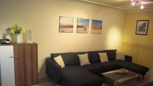Ein Wohnzimmer mit einer schwarzen Couch, einem Holzkabinett und einem Fliesenboden.
