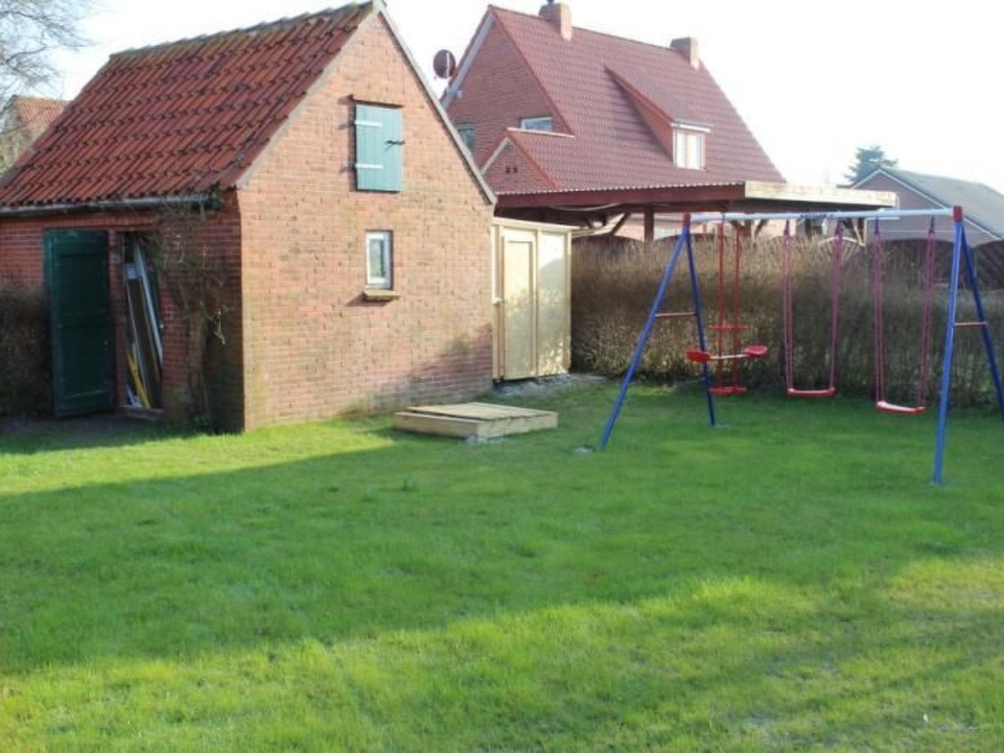 A brick house with a red-tiled roof, a small attached garage, and a swing set in the yard.