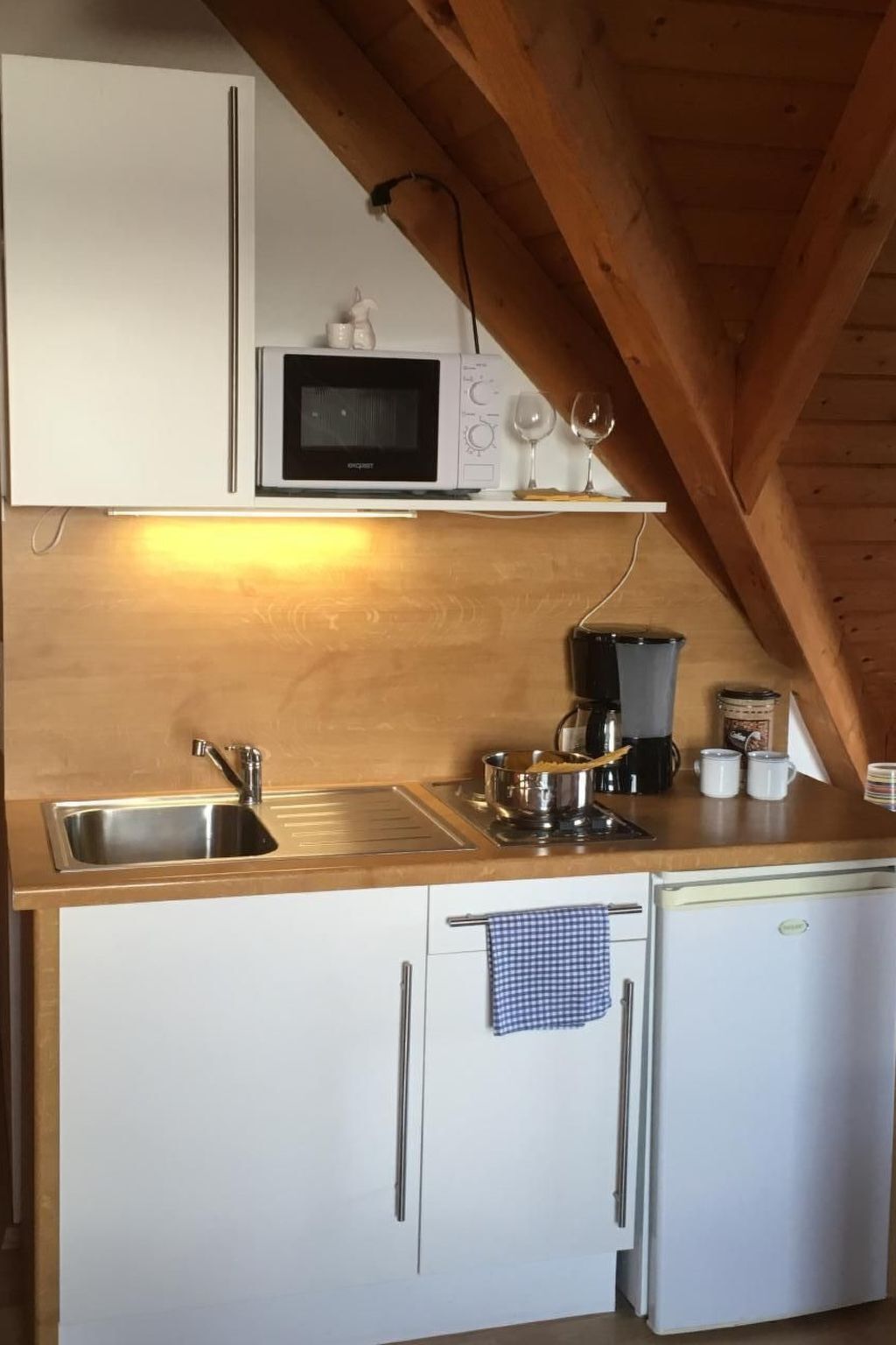 Una cocina compacta con microondas, lavamanos y cafetera.
