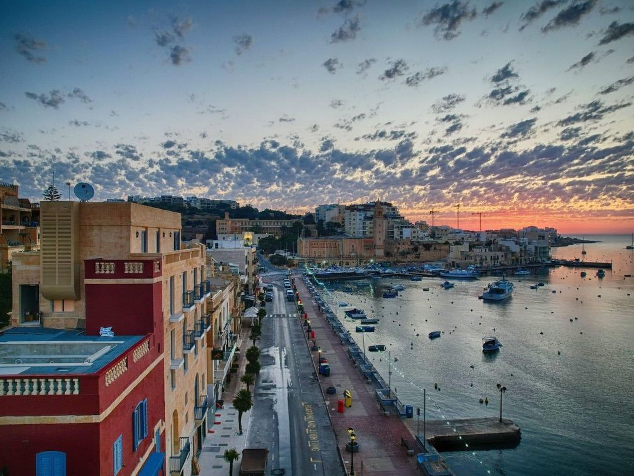 Un paysage urbain côtier avec un port de plaisance, des bâtiments le long du front de mer et un ciel au coucher du soleil.