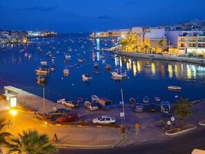Un puerto deportivo con barcos amarrados, un estacionamiento y edificios a lo largo del frente marítimo.