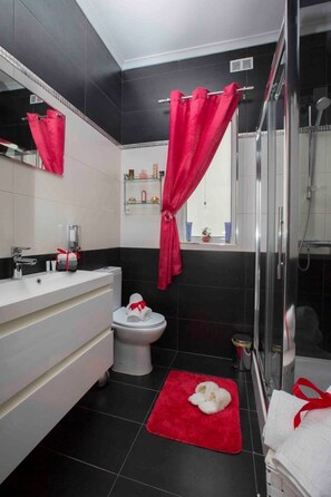 A modern bathroom with a white vanity, a toilet, a shower area, and a red bath mat. - Schöne, strandnahe Ferienwohnung in San Tumas by Interhome (Marsascala)