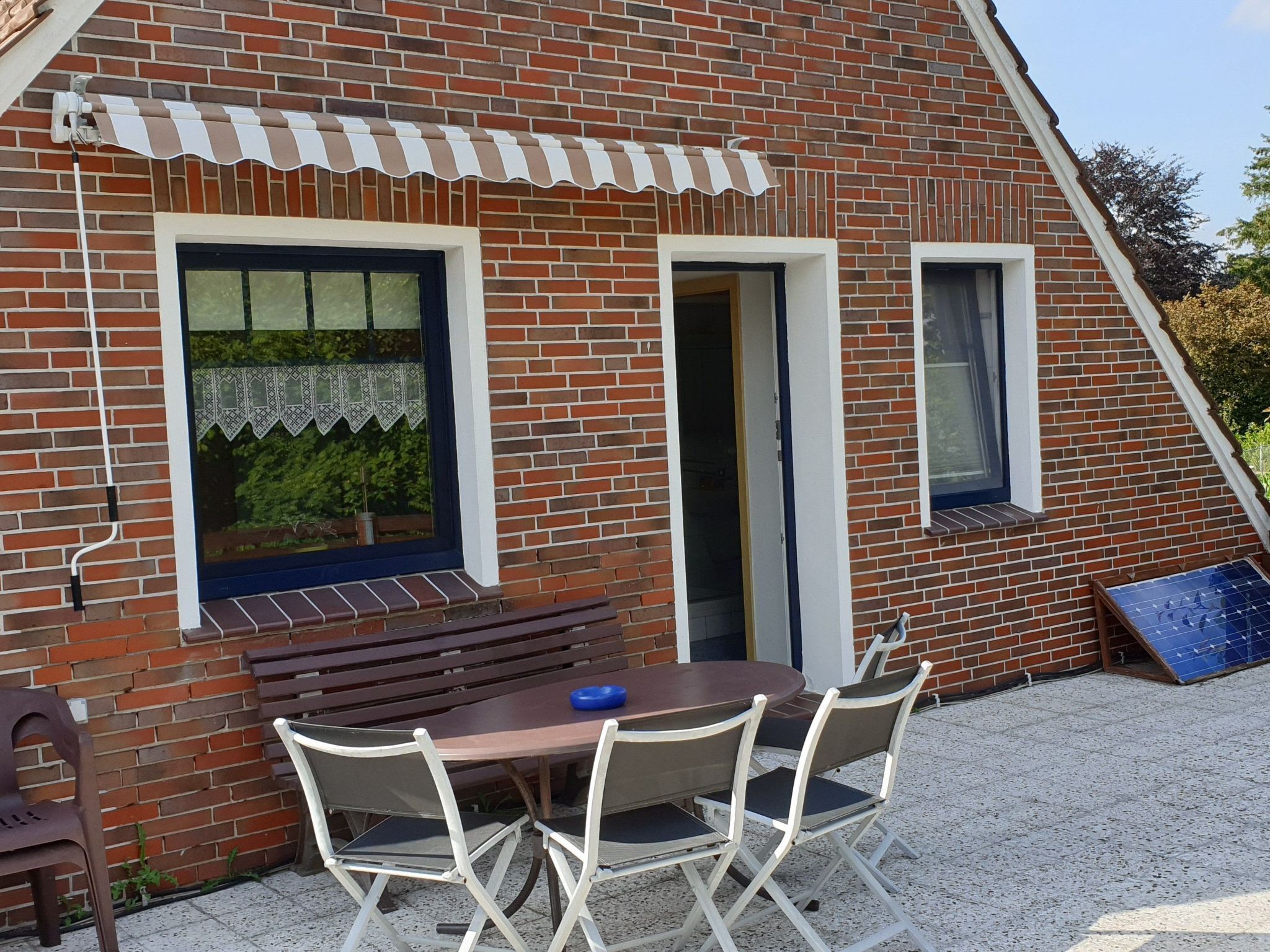 A brick building with a sloped roof, a small patio with a table and chairs, and a bench.