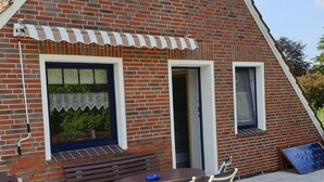 Un bâtiment en briques avec un toit en pente, un petit patio avec une table et des chaises, et un banc.