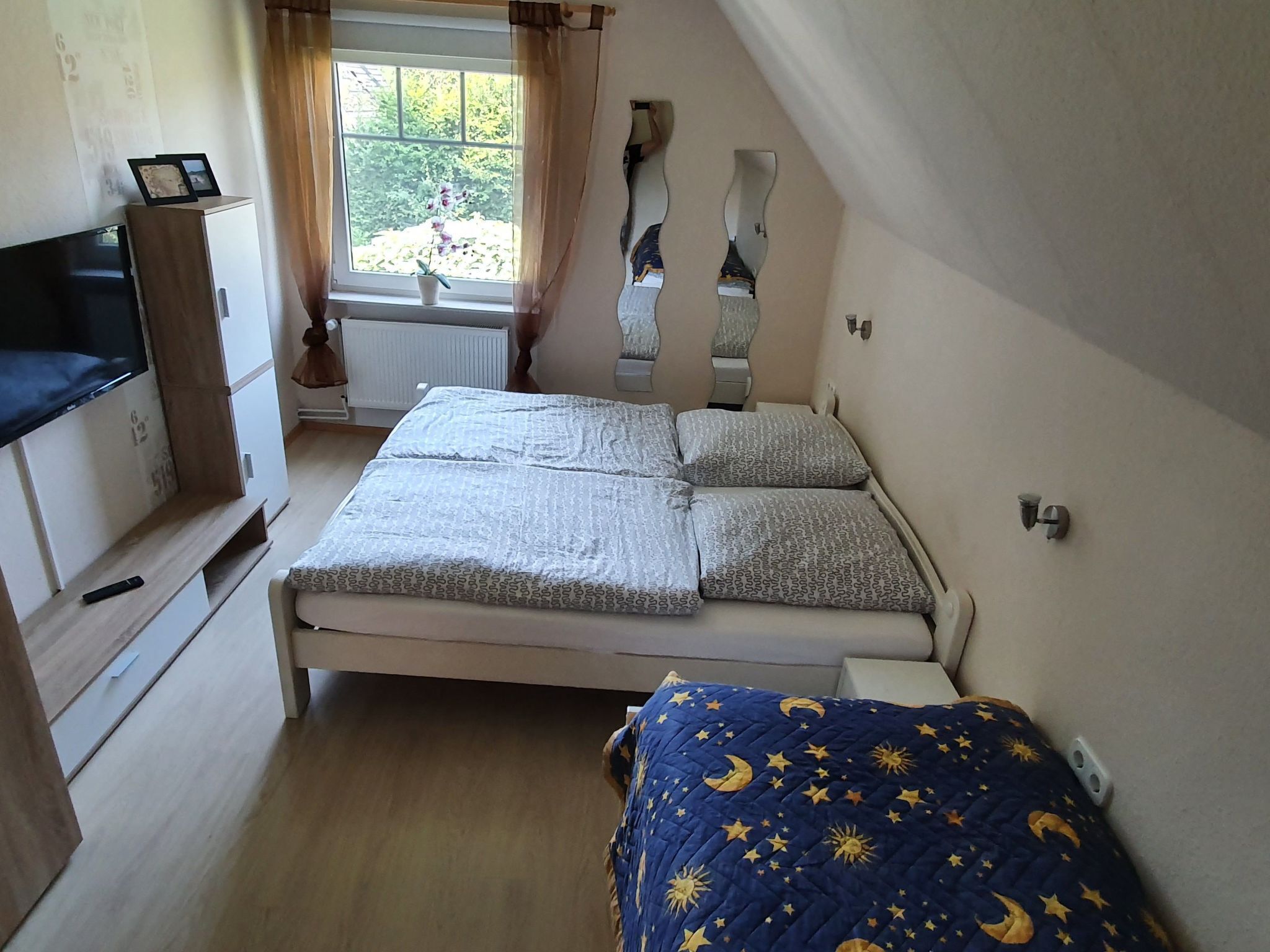 Une petite chambre confortable avec un lit simple, une télévision et une fenêtre avec des rideaux.