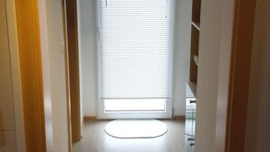 Un couloir étroit, avec une porte sur la gauche et une fenêtre avec des stores sur la droite.