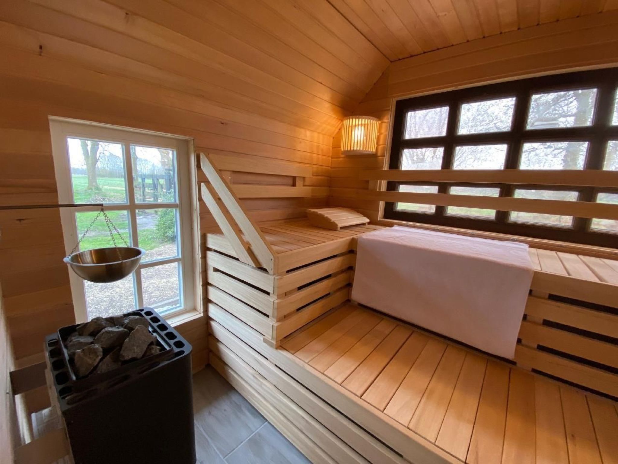 Un sauna en bois, avec un banc, une fenêtre et un récipient métallique suspendu.