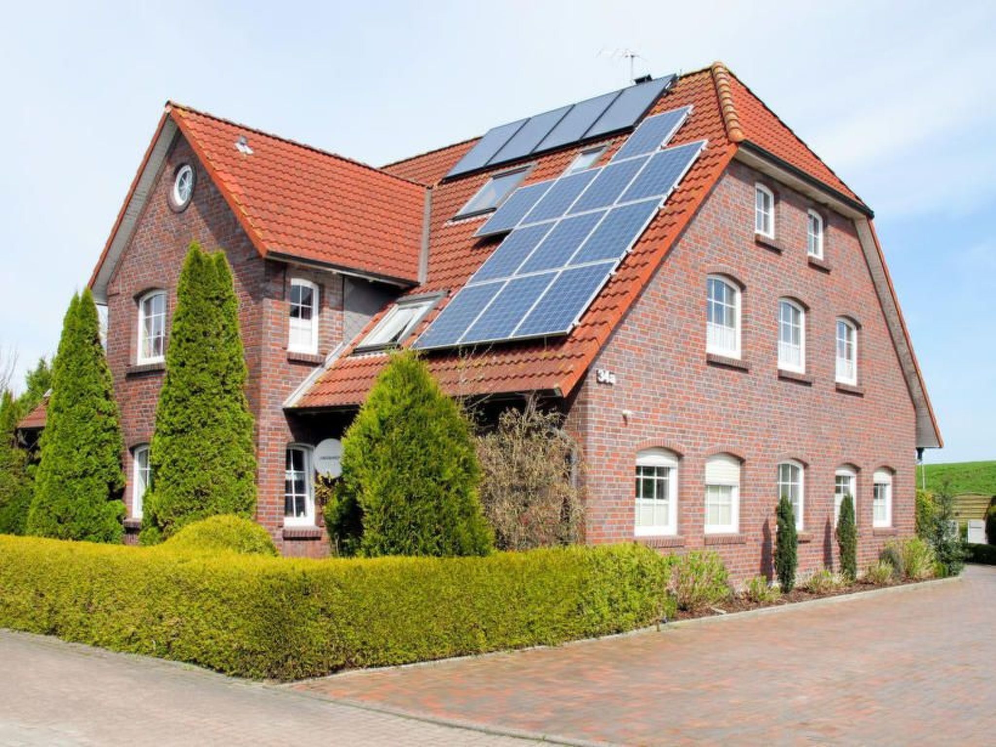 Una casa de ladrillo de dos pisos con paneles solares en el techo, rodeada de setos y árboles bien cuidados.
