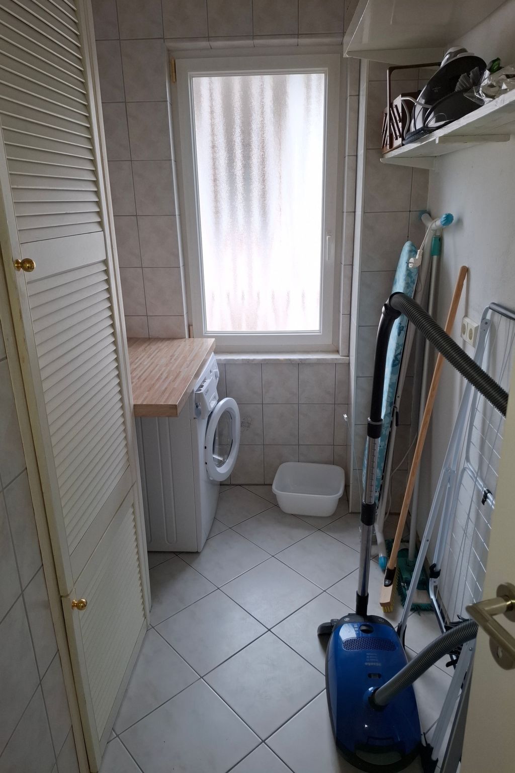 Een kleine badkamer met een wasmachine, toilet en raam voorzien van gordijnen.