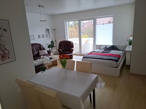A modern, well-lit living room with a dining area, a large bed, and a sliding glass door leading to an outdoor patio. - Private Ferienwohnung in Nordenham, großer Balko by Interhome (Abbehausen)