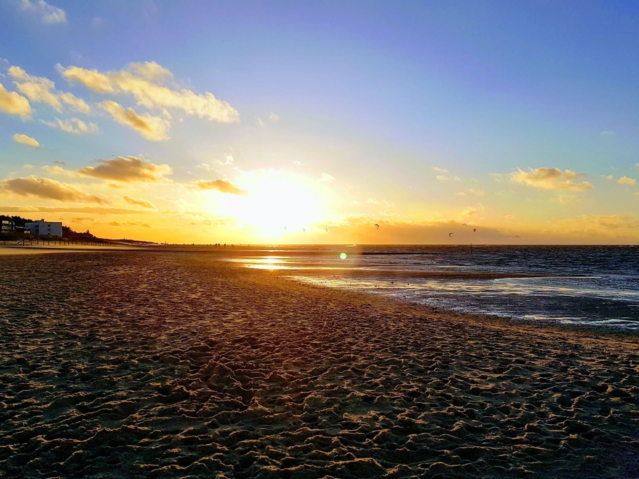 Ein Strand bei Sonnenuntergang, mit sandigem Ufer und einigen Gebäuden in der Ferne.