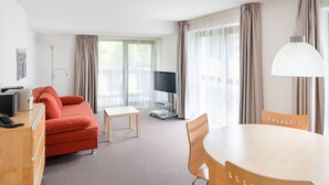 Ein modernes Hotelzimmer mit einem roten Sofa, einem Holztisch, einem Fernseher und einem großen Fenster mit Vorhängen.