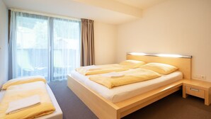 A hotel room with a bed, a bedside table, a chair, and a window with curtains. - Bohemia 2 in Gargellen by Interhome (Gargellen)