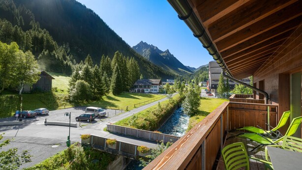 A balcony with a view of a mountain, a river, and a parking area. - Bohemia 2 in Gargellen by Interhome (Gargellen)