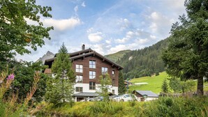 A modern building with a wooden facade, surrounded by lush greenery and a flowing stream. - Bohemia 2 in Gargellen by Interhome (Gargellen)