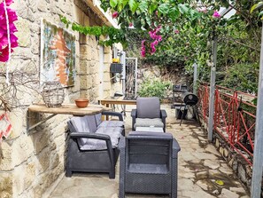 Een terras met rieten meubels, een tafel en een barbecue.