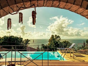 Une vue sur la piscine, avec un ciel dégagé, une terrasse en bois et une vue sur la mer.