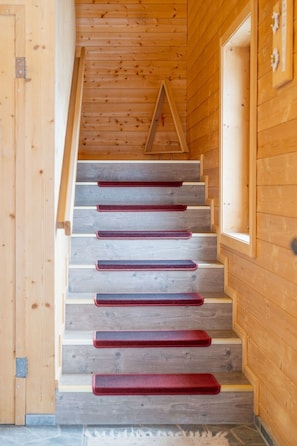 Eine Holztreppe mit roten Teppichläufern, die zu einem Schlafbereich führt.
