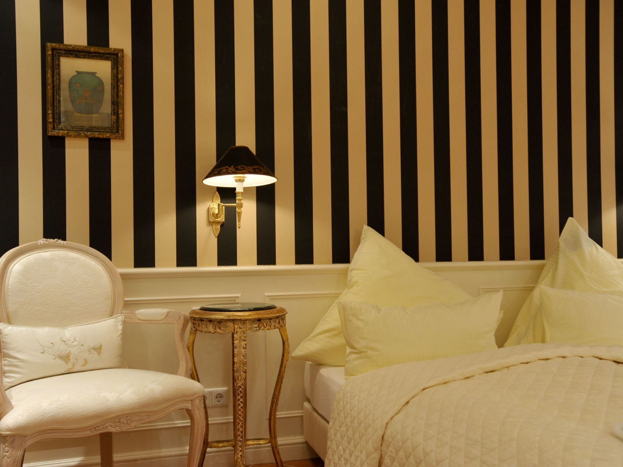 A room with a bed, a chair, a small table, and a wall-mounted lamp.