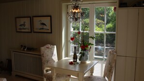 A dining area with a white table and floral chairs, a chandelier, and framed bird paintings on the wall. - Liiger Wal in Morsum by Interhome (Archsum)