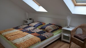 A small, single-bed room with a sloped ceiling and skylight, a bedside table with a lamp, and a wicker chair. - Appartement mit WLAN by Interhome (Hoppegarten)