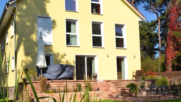 A yellow two-story house with a small pond in the foreground, surrounded by greenery and trees. - Appartement mit WLAN by Interhome (Hoppegarten)