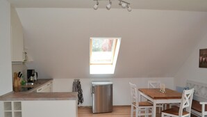 A compact kitchen with a window, a dining area with a wooden table and white chairs, and a built-in bench. - Appartement mit WLAN by Interhome (Hoppegarten)