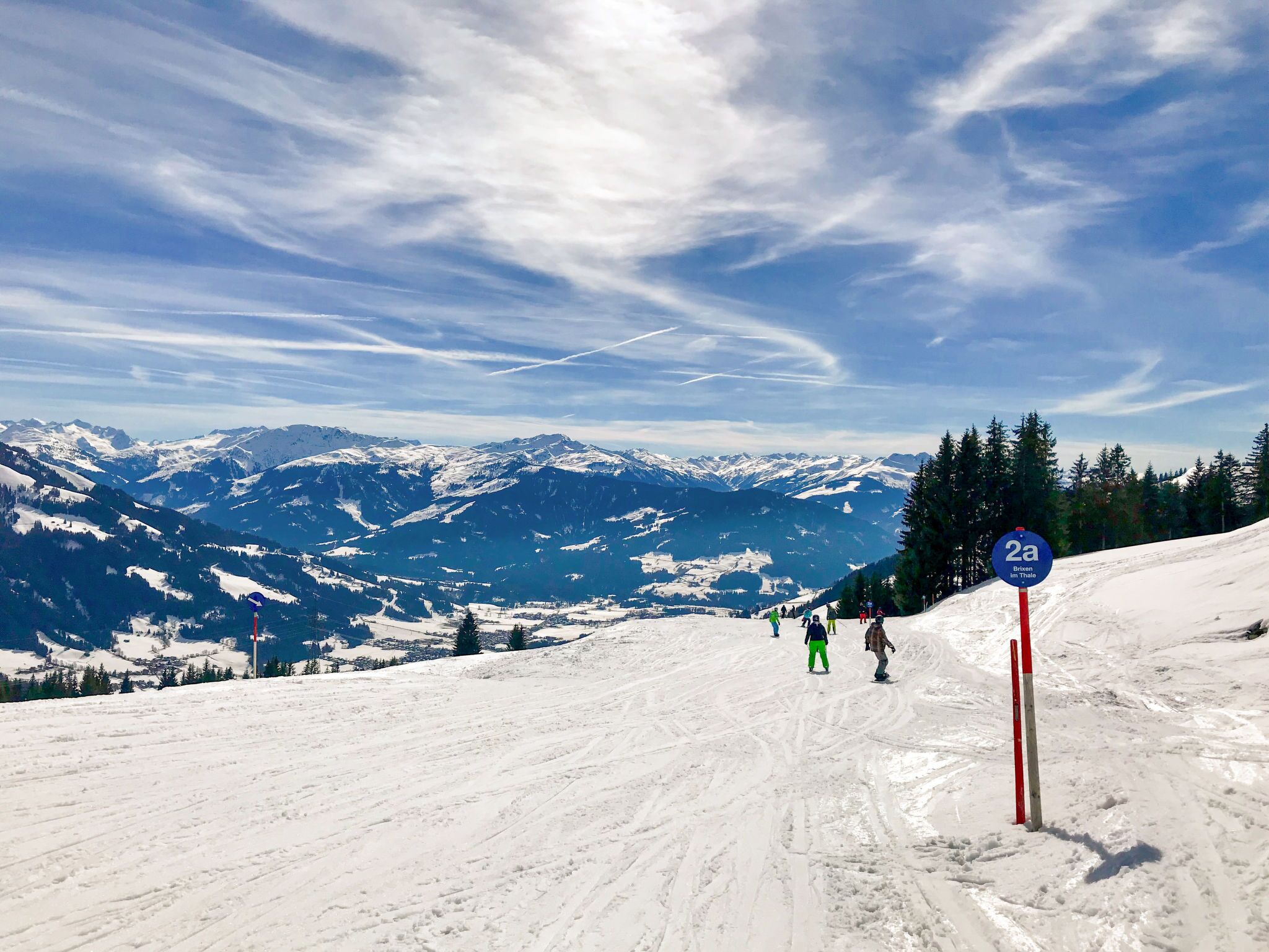 A snowy mountain slope with skiers and a sign indicating a ski trail.