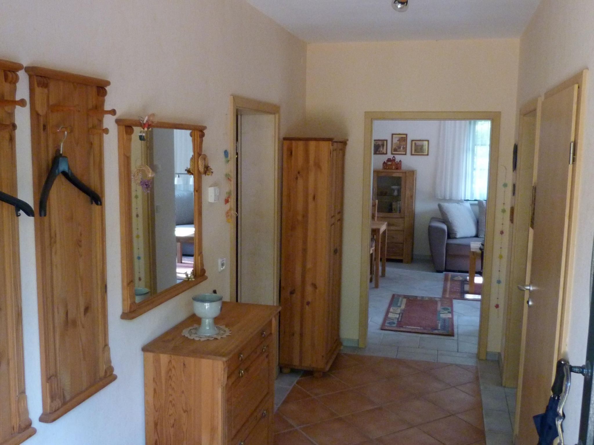 A hallway with wooden furniture, a mirror, and a door leading to a living area with a sofa and a cabinet.