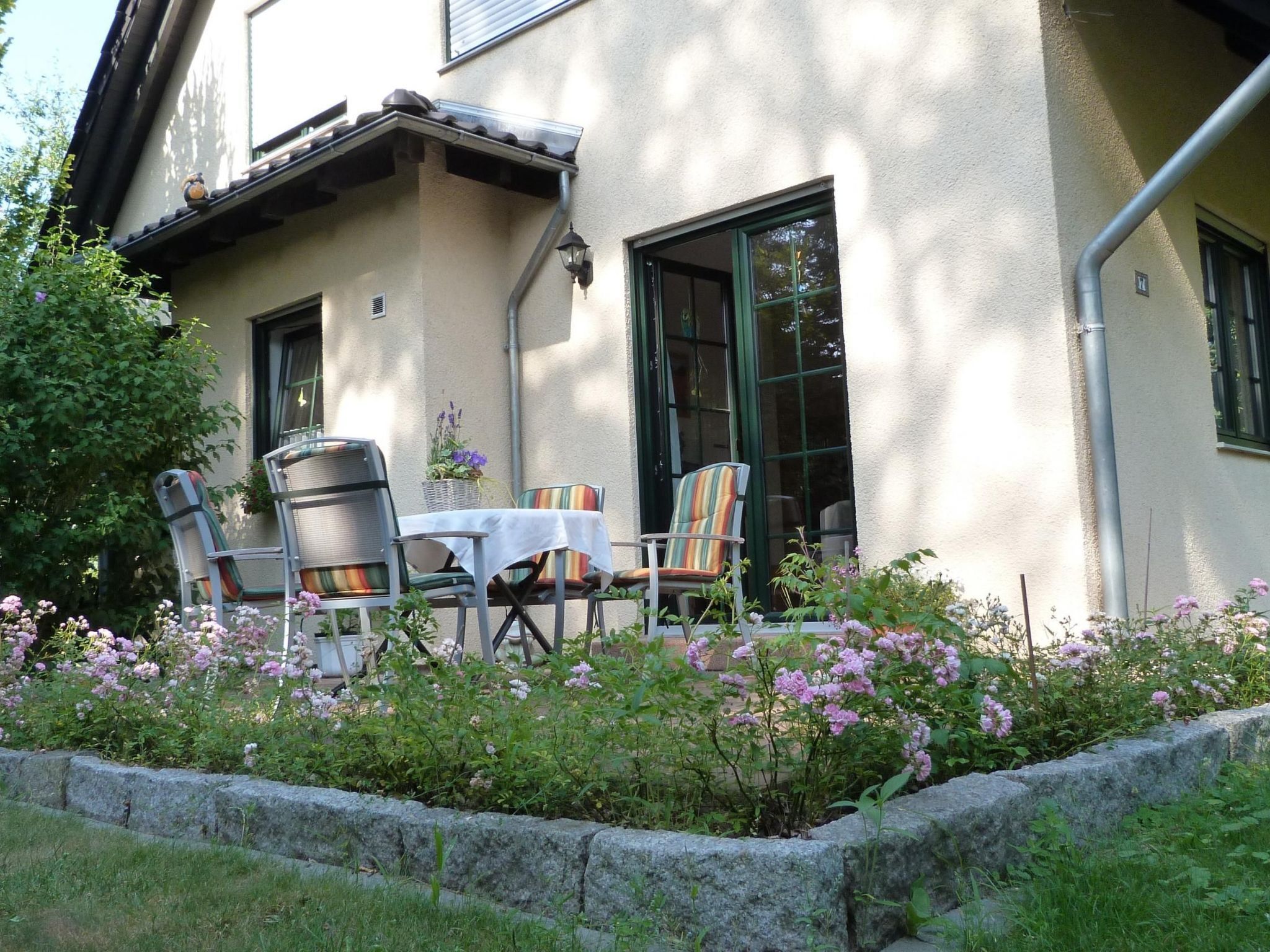 A patio with a table and chairs, surrounded by a stone wall and flowering plants.