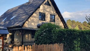 Perinteinen talo, jossa on kalteva katto, puinen aita ja runsas viherkasvillisuus.