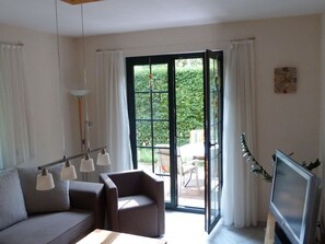 Un salon moderne comprenant un canapé, des fauteuils, un téléviseur et une porte-fenêtre coulissante donnant sur un espace extérieur.