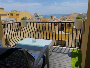 Un balcon avec une table et des chaises, donnant sur une zone côtière avec des bâtiments et une vue sur la mer.