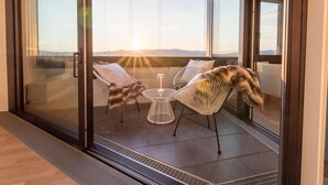A balcony with a glass door, two wicker chairs, a small round table, and a view of the landscape. - Skyflats Hills View by Interhome (Vienna)
