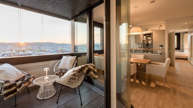 A modern hotel room with a city view, a balcony with seating, and a kitchenette. - Skyflats Hills View by Interhome (Vienna)